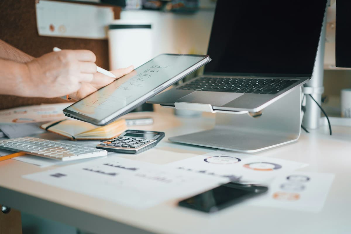 A desk with a laptop, calculator and a tablet used to review figures